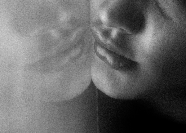 A monochrome close up of a woman’s face and nose pressed against a pane of glass, mirroring her reflection back at her.